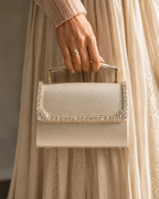 Model in champagne tulle dress holding Bare Silk crystal-embellished mini top-handle bag by House of Shine, gold ring detail, gold-polished hardware, saffiano exterior, Bijou Edit.