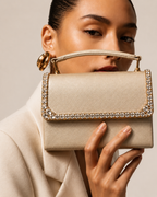 Model in ivory blazer holding Bare Silk crystal-embellished mini top-handle bag by House of Shine up near her face, gold hoop earring, gold-polished hardware, saffiano exterior, Bijou Edit.