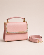 Blush pink satin mini top handle bag with crystal trim flap and detachable shoulder strap laid beside it, The House of Shine Bijou Edit