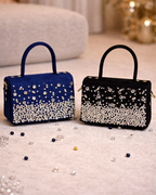 Estrella satchel by House of Shine in Midnight navy and Onyx black both colourways styled on cream surface with scattered crystals and pearls warm gold background