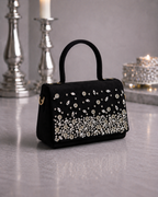 Estrella hand-embellished onyx black butter suede satchel by House of Shine front angle view with cascading rhinestone constellation pattern silver candlesticks and candlelight in background