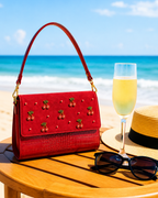The Amarena hand embroidered bag styled on a beach table with champagne, a luxury embroidered satchel for summer