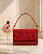 The Amarena hand embroidered designer handbag beside a scoop of cherry gelato on marble