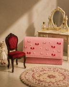 Bambola pink structured mini bag by The House of Shine with hand-embroidered bows and pearl accents, styled in a miniature dollhouse setting.