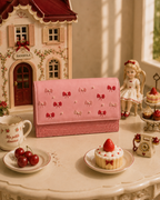 Bambola pink hand-embroidered mini bag styled in a whimsical dollhouse tea-party scene with cherries and a strawberry dessert.