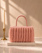 Blush pink Cascade Satchel with fringe embroidery beside a lit taper candle on marble
