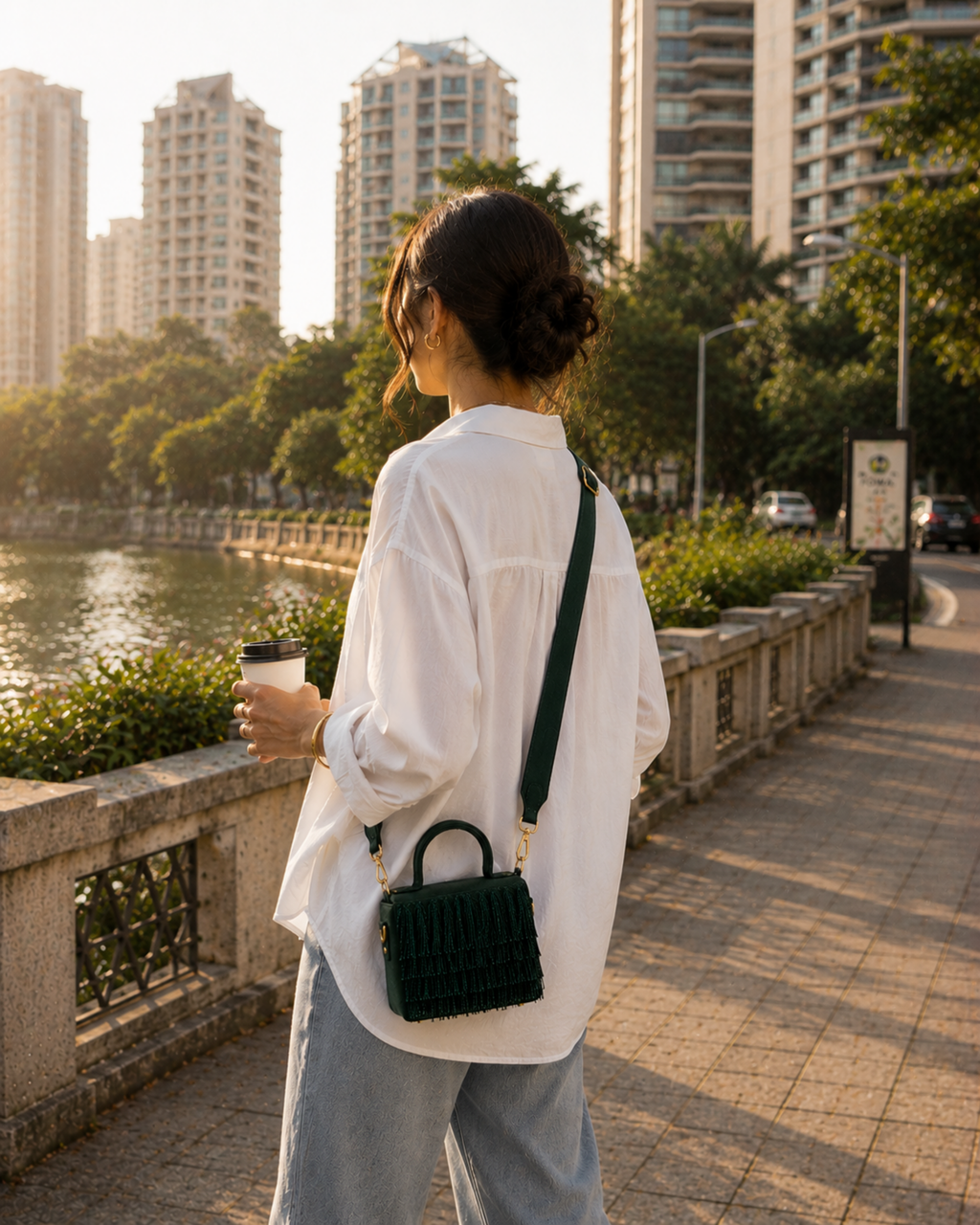 Woman walking along a riverside promenade carrying green Cascade Satchel crossbody