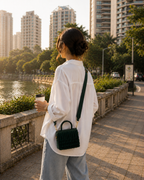 Woman walking along a riverside promenade carrying green Cascade Satchel crossbody