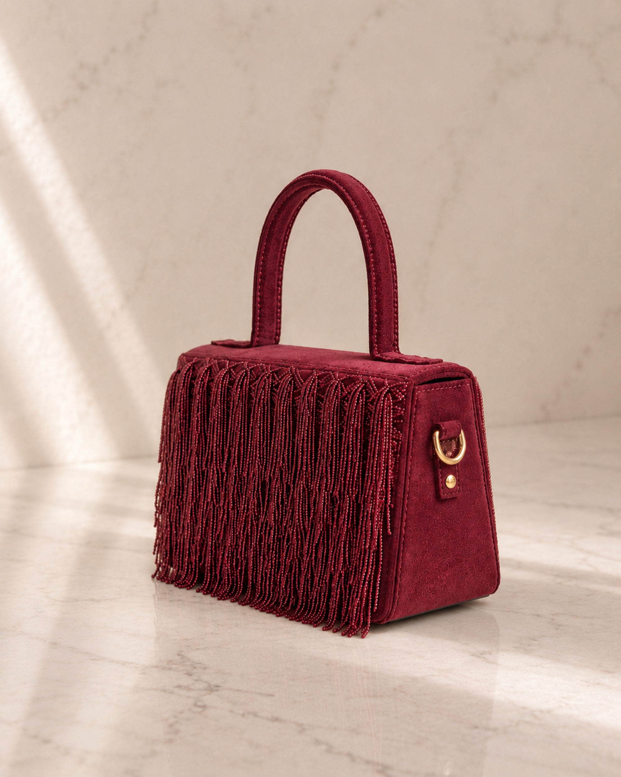 Close-up detail of maroon Cascade Satchel showing fringe and gold hardwareClose-up detail of maroon Cascade Satchel showing fringe and gold hardware