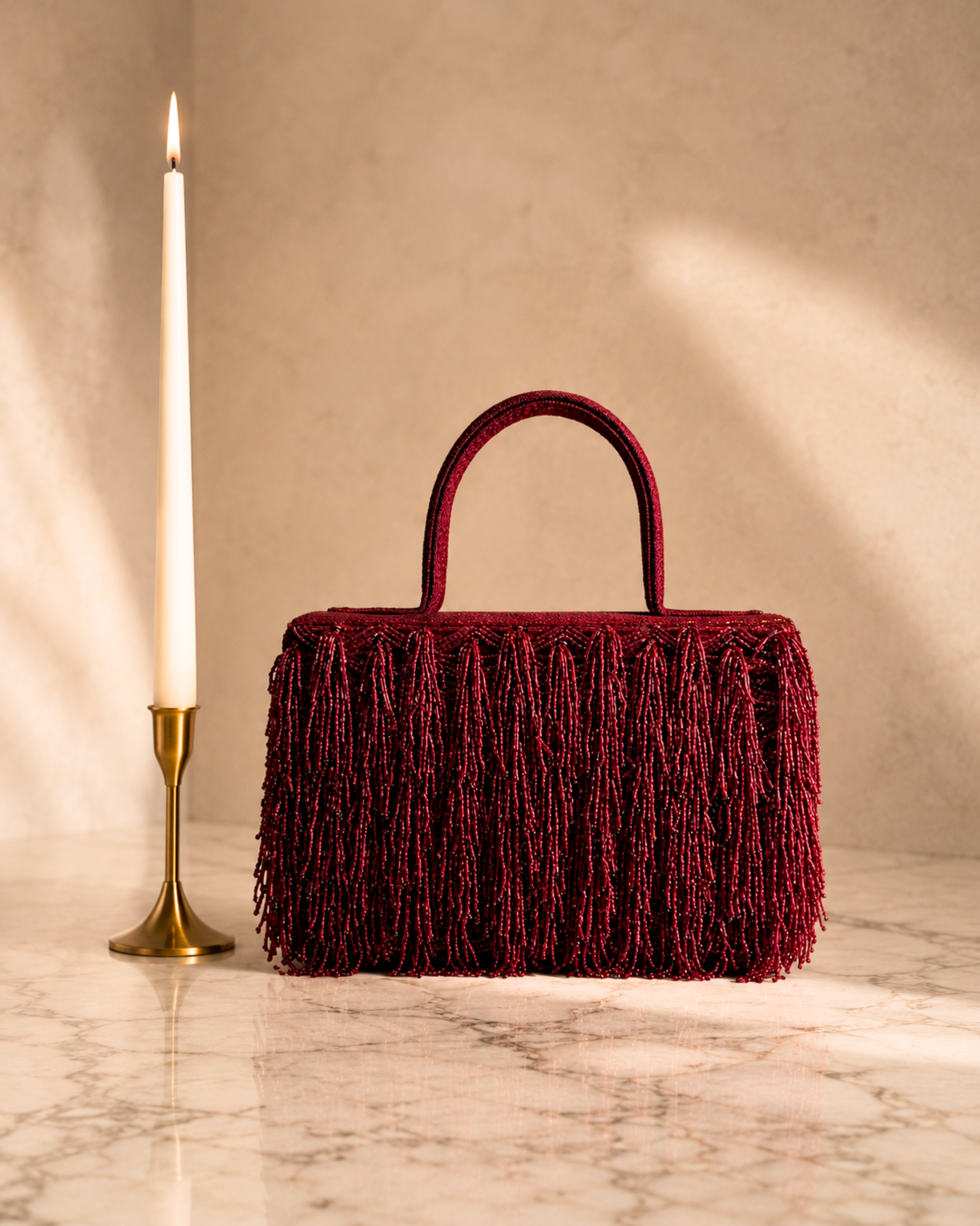 Maroon Cascade Satchel with beaded fringe embroidery, front view beside a taper candle