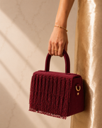Woman's hand holding maroon Cascade Satchel against a gold satin backdrop