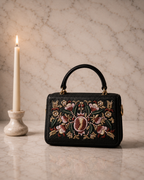 The House of Shine Florence hand-embroidered black satchel with pomegranate floral motif in silk thread and pearl beads, front view on marble surface