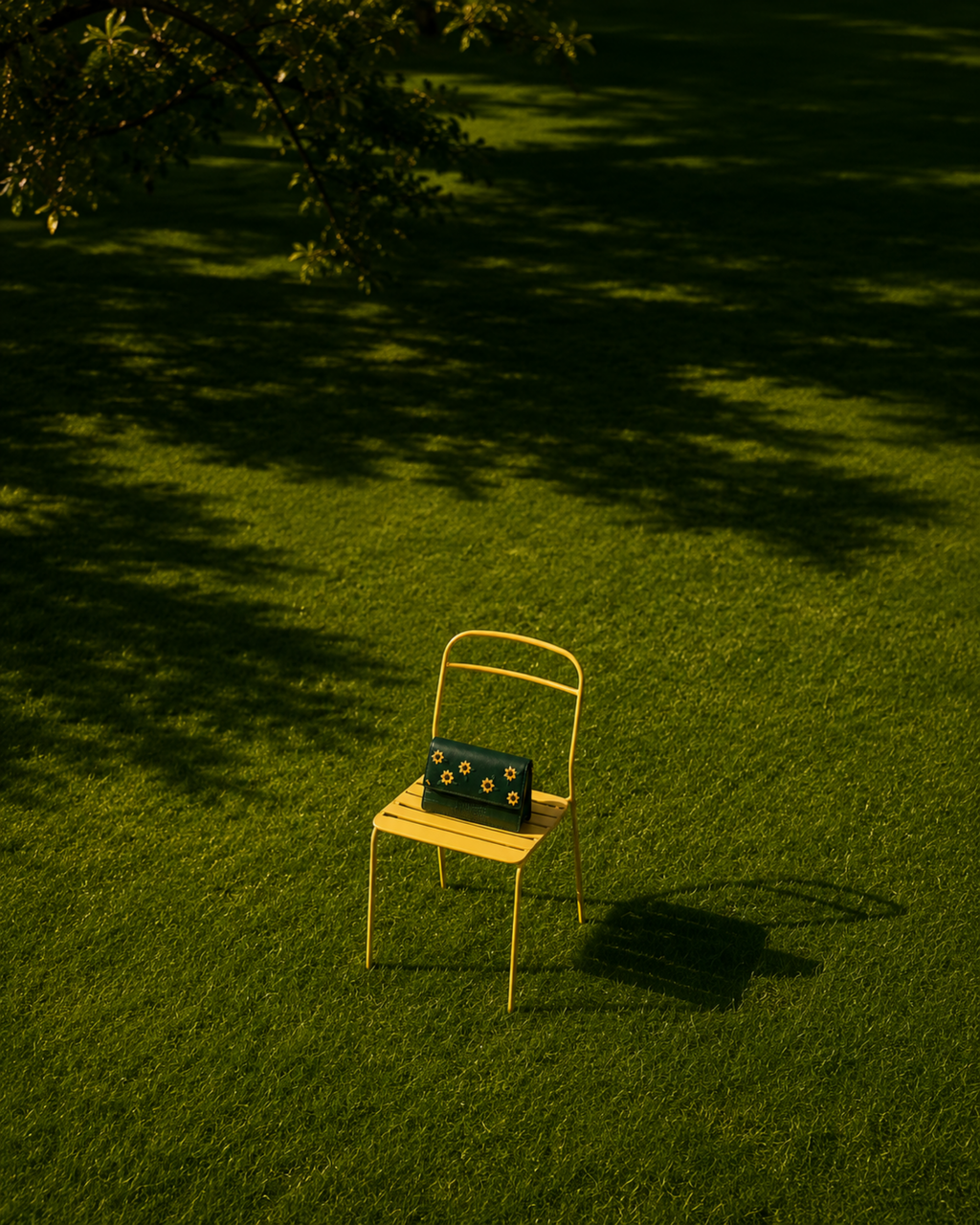 Girasole Mini Gelato green embroidered bag with yellow floral motifs displayed on a yellow chair in a sunlit garden.