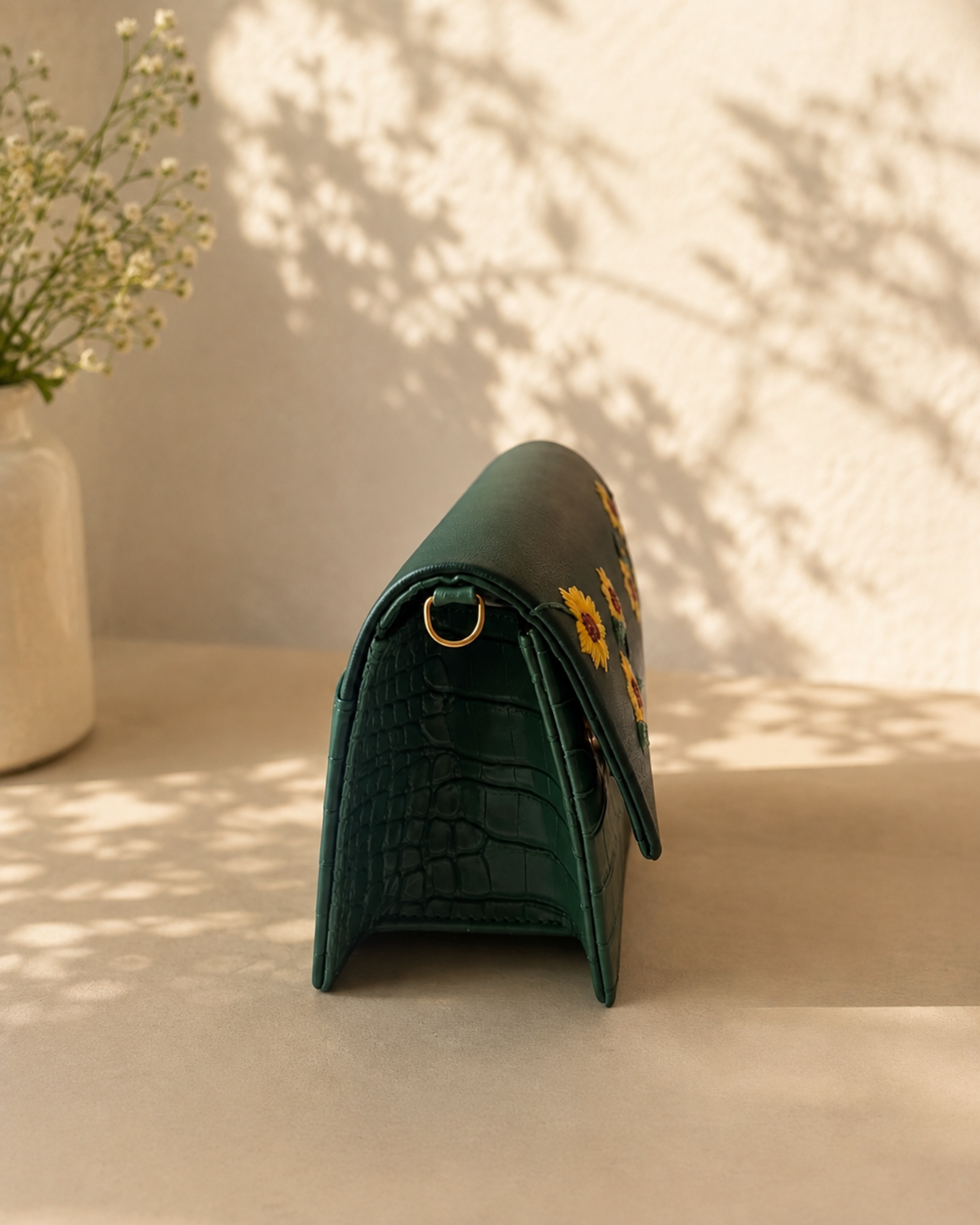 Side profile of the Girasole green mini bag showing its structured silhouette, crocodile-textured gusset and gold-tone D-ring.