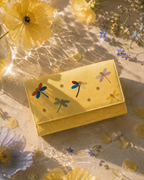 Close-up of the Libellula butter-yellow mini bag with hand-embroidered dragonflies and croc-textured base in soft sunlight.
