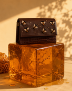 Miele brown bee embroidered mini bag by The House of Shine displayed on a translucent amber pedestal with crocodile-textured detailing.