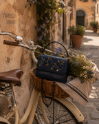Mirtillo hand embroidered bag India nestled in a bicycle basket filled with wildflowers on a cobblestone street