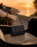 Gloved hand holding the Mirtillo hand embroidered bag in a vintage carriage at golden hour by the sea