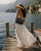 Woman in a flowing white dress carrying the Mirtillo hand embroidered bag on a lakeside dock, luxury handbag India
