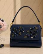 Mirtillo hand embroidered bag India styled on a marble surface with fresh blueberries and a pastel dessert