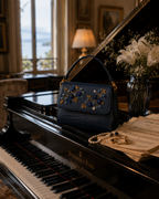 Mirtillo hand embroidered designer handbag on a grand piano with pearls, gold rings, and sheet music