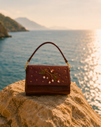 Hand embroidered designer handbag — The Nocciola shoulder bag styled on coastal rock at golden hour