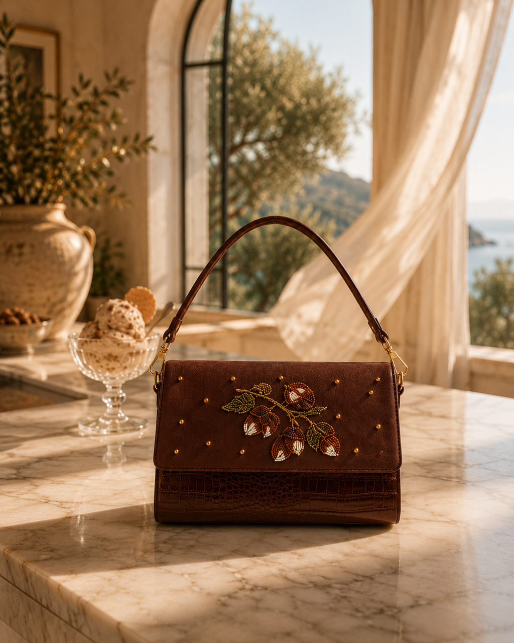 Hand embroidered designer handbag — The Nocciola on a sunlit terrace counter with olive tree view