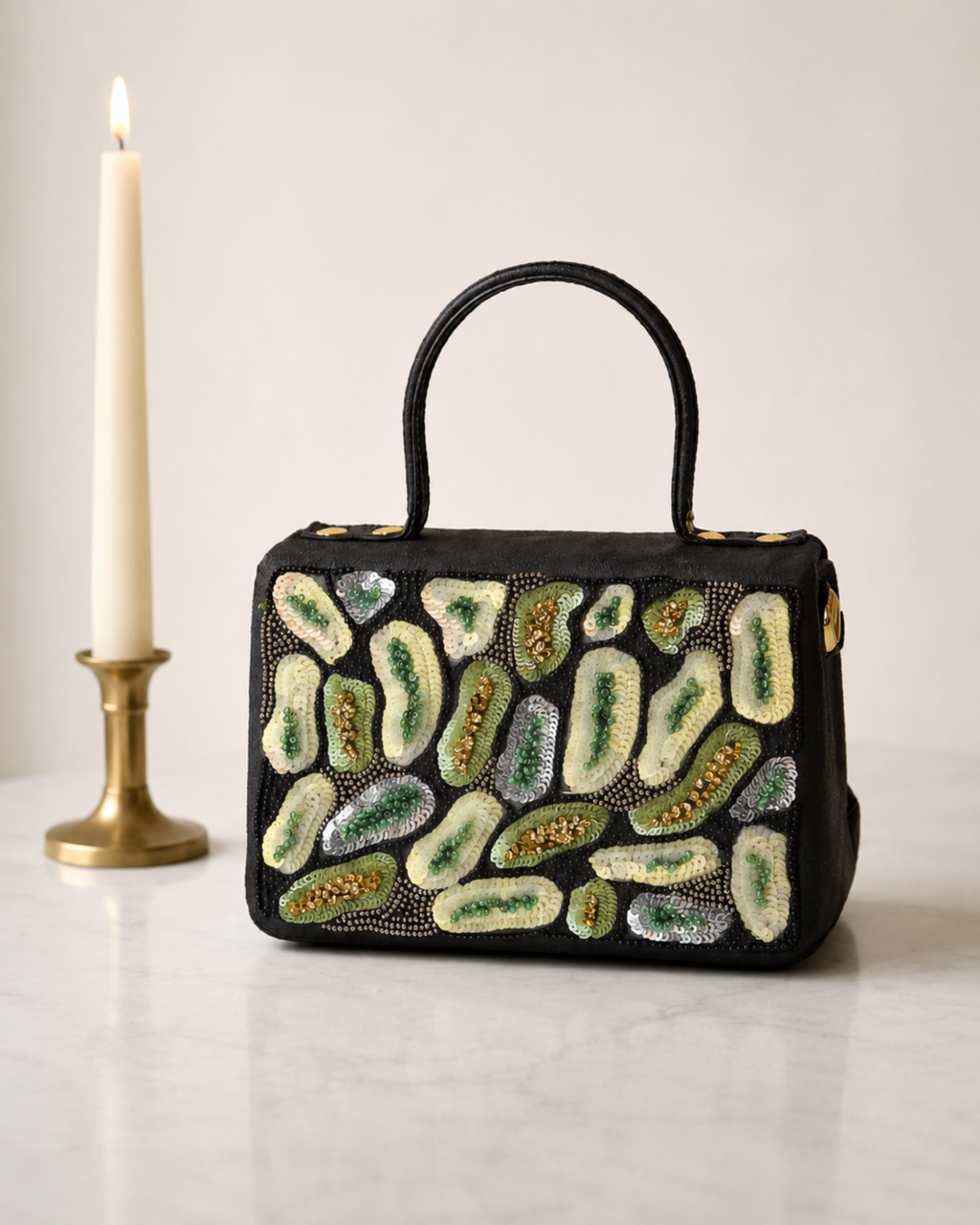The House of Shine Prisma hand-embroidered black satchel with green and ivory sequin and bead motifs, front view on marble surface