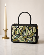 The House of Shine Prisma hand-embroidered black satchel with green and ivory sequin and bead motifs, front view on marble surface