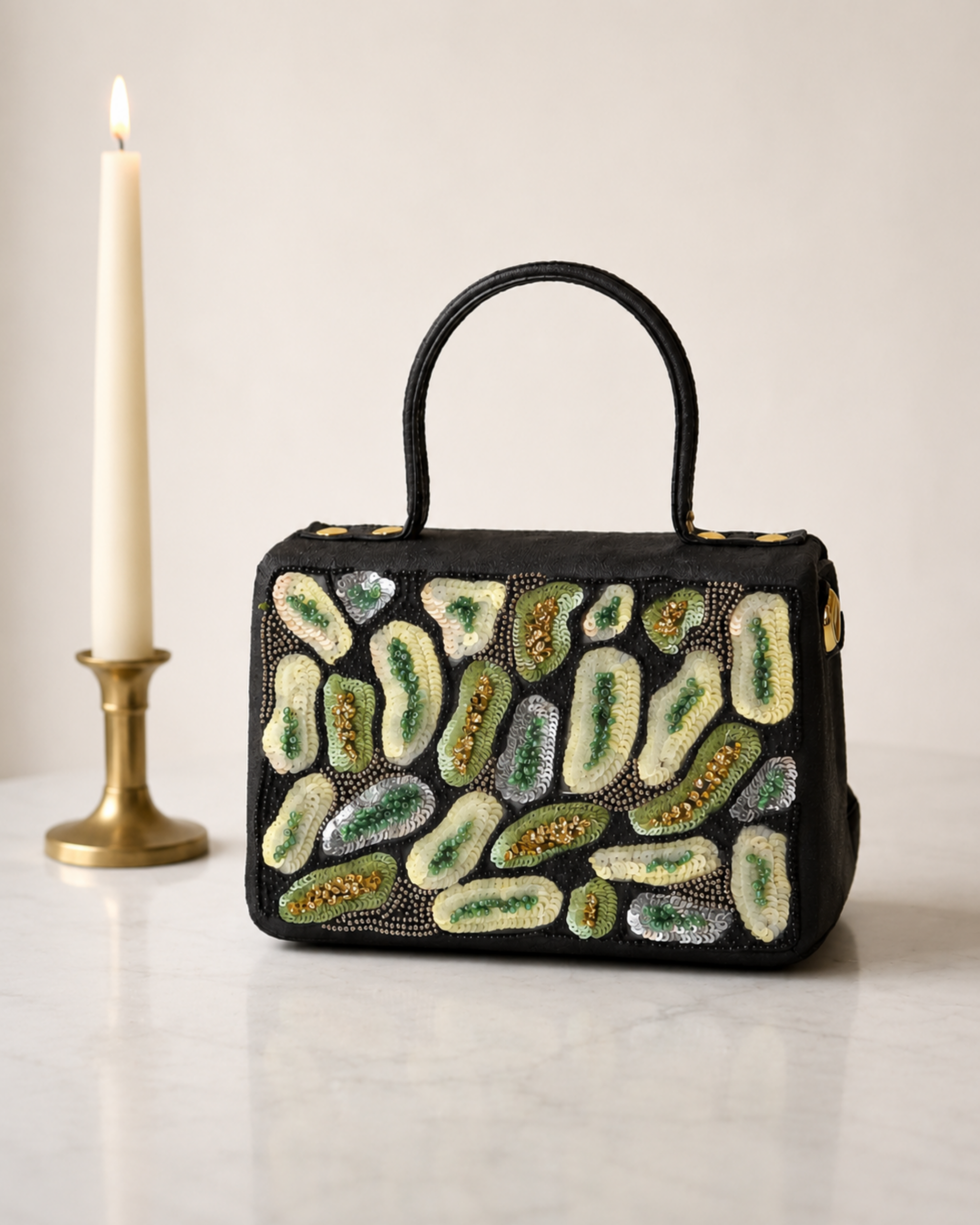The House of Shine Prisma hand-embroidered black satchel with green and ivory sequin and bead motifs, front view on marble surface