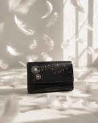 Soffio structured black mini bag surrounded by floating white feathers in a soft sunlit editorial setting.