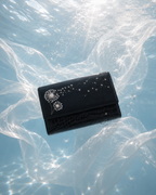 Soffio black dandelion embroidered mini bag surrounded by flowing translucent fabric in a dreamy blue underwater-inspired setting.