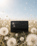 Soffio black structured mini bag with hand-embroidered dandelions photographed in a dreamy dandelion field.