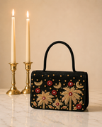 House of Shine Tropical Moonbeam Satchel in black velvet, front view of gold and red hand embroidered palm tree and crescent moon design with brass candle holders