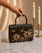 Hand holding House of Shine Tropical Moonbeam Satchel in olive suede by top handle, gold zardozi embroidery with red floral and crescent moon motifs