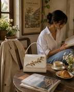 Zagara ivory floral bag styled beside a woman reading at a relaxed Italian café
