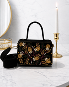 Nocturne Satchel in black with gold zardozi vineyard embroidery styled with gold candlestick and mirror on marble, Noir Atelier by The House of Shine