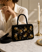 Nocturne Satchel on marble table beside woman in cream shirt with gold chandelier earrings and lit candle, Noir Atelier by The House of Shine