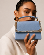 Model in ivory blazer holding Something Blue crystal-embellished mini top-handle bag by House of Shine up near her face, gold hoop earrings, gold-polished hardware, saffiano exterior, Bijou Edit.
