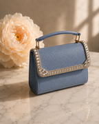 Something Blue crystal-embellished mini top-handle bag by House of Shine, angled shot on marble with blush peony, gold-polished hardware, saffiano exterior, Bijou Edit.